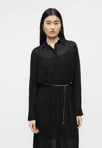 Μαύρο διαφανές πουκαμισοφόρεμα με γιακά, μακρυά μανίκια και σφιχτή μέση. Διαθέτει ασημένια αλυσίδα-ζώνη για επιπλέον λεπτομέρεια.