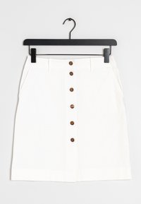 Jupe en denim blanc suspendue à un support noir, dotée d'une fermeture à boutons sur le devant avec des boutons marron, de poches latérales et d'une coupe droite.