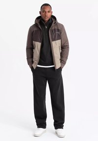 Vadderad jacka med huva, med en beige och brun färgblockdesign. Mjuk textur och dragkedjestängning, kombinerad med svarta byxor och vita sneakers.
