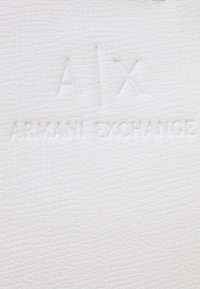 Bílé kůže s texturovaným povrchem s embosovanými brandingovými detaily: "A|X" a "ARMANI EXCHANGE." Minimalistický design.
