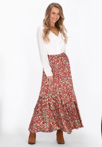 Fustă maxi florală în roșu cu modele verzi și albastre; țesătură ușoară, design în straturi, asortată cu o bluză albă și cizme până la gleznă maro.