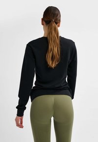 Zwarte sweatshirt met lange mouwen en geribde manchetten, gecombineerd met olijfgroene leggings met een gestructureerd patroon en een getailleerd ontwerp.