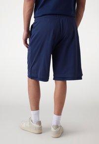 Marineblå åndbare mesh sportshorts med elastisk talje, sidelommer og en let løs pasform. Hvide sneakers og sokker synlige.