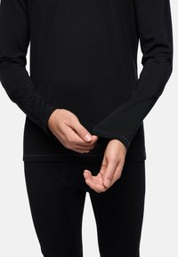 Zwarte langemouwen top van gladde stof. Heeft aansluitende mouwen met duimgaten en contrasterende stiksels langs de zoom.