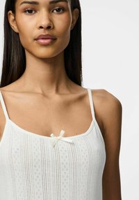 Camiseta blanca con delicadas rayas verticales y patrones de ojales, con finas tirantes ajustables y un pequeño lazo de satén en el centro.