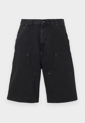 Mustad teksapüksid, millel on mitu eesmine taskut ja vööaasad, millel on neetide detailid ja nupuga kinnis.