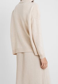 Pull en tricot beige avec un col montant, des épaules tombantes et des poignets côtelés, associé à une jupe côtelée assortie. Texture douce, coupe décontractée.