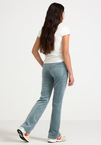 Světle modré sametové kalhoty s hladkým povrchem, doplněné zadními kapsami. V kombinaci s bílou úzkou košilí a vícebarevnými teniskami.