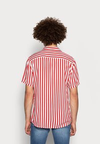 Camiseta de manga corta a rayas horizontales rojas y blancas con cuello clásico y detalle de canesú trasero. Tela ligera, ajuste holgado.