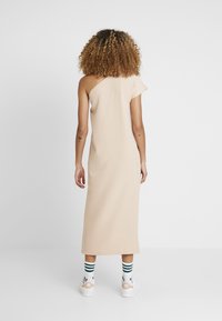Béžové šaty na jedno rameno vyrobené z lehké tkaniny, s rovnou siluetou, střední délkou a jemnou texturou.