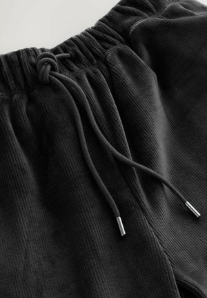 Svarta ribbade joggers med resårmidja och dragsko, inklusive silverfärgade metallaglets i ändarna av dragskon.