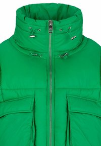 Grüne Steppjacke mit hohem Kragen, Front-Reißverschluss und zwei großen aufgesetzten Taschen. Mit Kordeln und metallischen Akzenten versehen. Weicher Stoff.