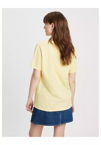 T-shirt z krótkim rękawem, żółty, bawełniany, o luźnym kroju, połączony z dżinsową spódnicą. Prosty design bez widocznych logo lub wzorów.