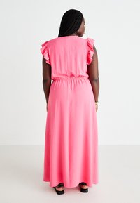Rosa maxiklänning med volangaxlar, elastisk midja och en slät yta, som når ner till anklarna med en rak siluett.