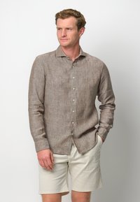 Camicia in lino marrone con colletto button-down, maniche lunghe e tasche frontali, abbinata a pantaloni corti beige chiaro. Design casual e testurizzato.