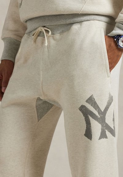 Lys grå joggebukser med et stort mørkegrå logo, kontrasterende grå detaljer ved knærne, og et elastisk liv med snor.