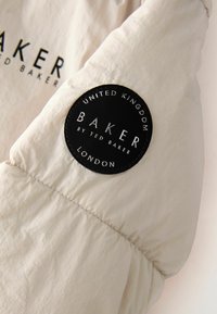 Bežna tkanina ima šav sa prošivenom linijom i okruglu crnu oznaku na kojoj piše "BAKER by TED BAKER" i "UNITED KINGDOM" u bijelom slovima.