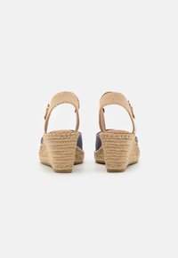 Sandalias cuña con una correa trenzada de color beige y cuerpo de tela azul, con un tacón de esparto texturizado en color natural y hebilla ajustable.