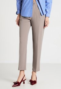 Pantalon beige ajusté avec une texture lisse et une coupe slim, associé à des escarpins en vernis bordeaux avec un détail en nœud.