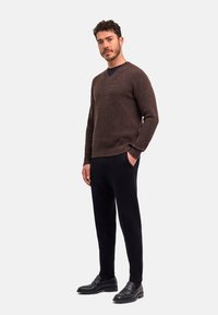 Maglione a V in maglia marrone abbinato a pantaloni neri e scarpe slip-on nere, con una superficie testurizzata e un design aderente.