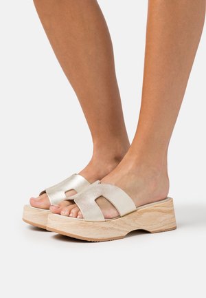 Sandales plateformes argentées métalliques avec une semelle en bois, design ouvert au niveau des orteils, et larges sangles avec des accents découpés.