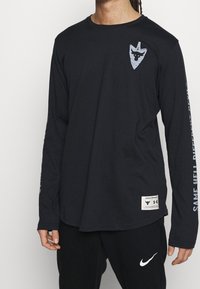 Czarna koszula z długim rękawem, wykonana z bawełny, z okrągłym dekoltem. Posiada graficzne logo na klatce piersiowej oraz napis wzdłuż rękawa.