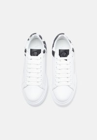 Λευκά αθλητικά παπούτσια με λείο δερμάτινο επάνω μέρος, στρογγυλή μύτη, κορδόνια στο μπροστινό μέρος και μαύρο λογότυπο. Το εσωτερικό διαθέτει γκρι και λευκή φόδρα με πουά σχέδιο.