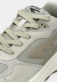 Jasnoszare buty sportowe z siateczkowymi panelami, zamszowymi akcentami, płaskimi sznurowadłami i gumową podeszwą. Posiadają subtelną logo na języku i boku.