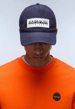 Navy baseball cap with a white "NAPAPIJRI geographic" logo on the front; orange sweatshirt with a round neckline and brand badge.