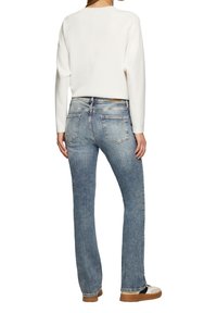 Lichtblauwe denim jeans met een rechte pasvorm, zichtbare zakken en een lichte vervaging, gecombineerd met een witte lange mouwtop en bruine schoenen.