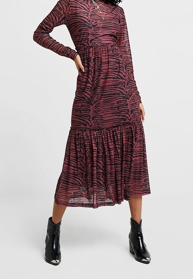 Femme portant une robe violette à manches longues avec des rayures noires de tigre et des bottines noires, debout avec une main sur la hanche.