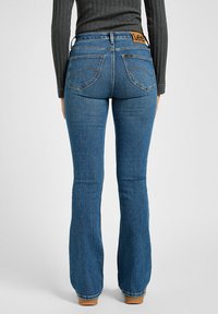 Blå denim med bootcut-fit och hög midja, med en läderetikett på baksidan, två bakfickor och en slät yta.