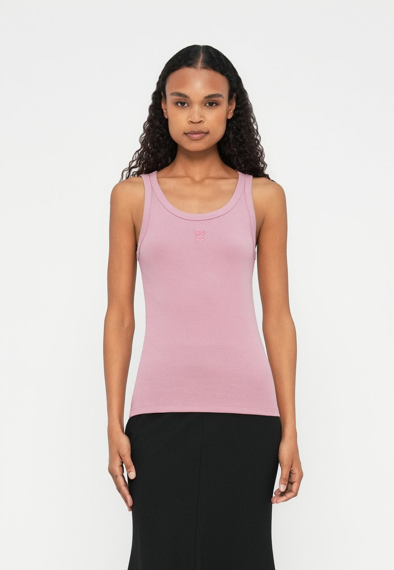 Lichtroze tanktop met een ronde halslijn, geribbelde textuur en een klein wit logo op de borst. Strak model met standaard schouderbanden.