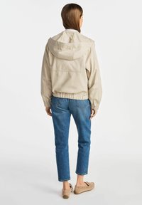 Jasnoszara kurtka z kapturem z elastycznymi mankietami i dołem, w połączeniu z niebieskimi, krótkimi dżinsami. Materiał wydaje się gładki z luźnym krojem.