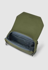 Sac rectangulaire vert olive avec extérieur texturé, rabat hexagonal, et intérieur bleu clair comprenant des poches organisatrices et une fermeture éclair.