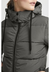 Kurtka puchowa w ciemnoszarym kolorze, z wysokim kołnierzem, czarnym zamkiem błyskawicznym i troczkami. Materiał gładki, z pikowanymi panelami.