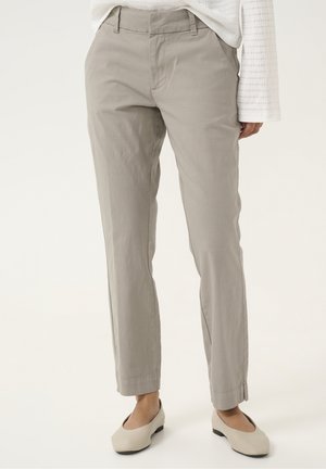 Beżowe spodnie o prostych nogawkach noszone z jasnobeżowymi balerinami i białą, teksturowaną bluzką z długim rękawem, przyciętą w talii i przy kostkach.