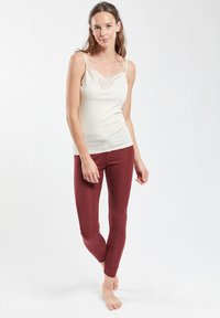 Top bianco senza maniche con pizzo e leggings bordeaux, entrambi aderenti, con una texture liscia e un design minimalista. Posizione a piedi nudi.