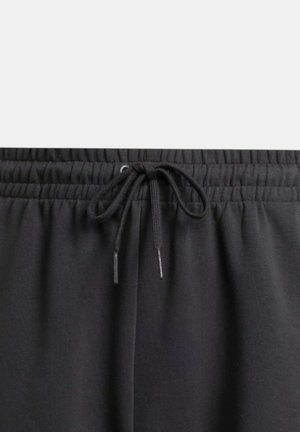 Los joggers negros con cintura elástica presentan un cierre ajustable con dos extremos sueltos, fabricados con una tela suave y texturizada que proporciona confort y movilidad.