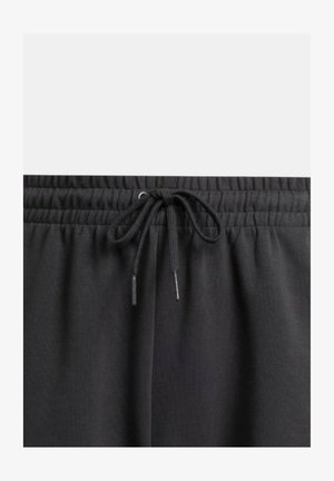 Los joggers negros con cintura elástica presentan un cierre ajustable con dos extremos sueltos, fabricados con una tela suave y texturizada que proporciona confort y movilidad.