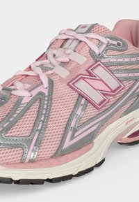 Chaussure de running New Balance rose avec tige en mesh, accents argentés réfléchissants, logo blanc et rose, et semelle blanche amortissante avec semelle extérieure noire.
