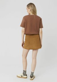 T-shirt marron oversize, mini-jupe en daim beige, chaussettes à imprimé animal, et baskets crème avec des accents marron. Design épuré et textures douces.