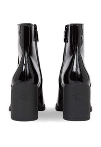 Botas de tobillo de charol negro con un alto tacón bloque, cierre de cremallera y detalle de logo en la parte trasera, presentando un acabado elegante y brillante.