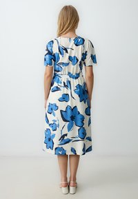 Bloemendress met blauwe en zwarte oversized bloemenpatronen op een crèmekleurige background, met een getailleerde taille en korte mouwen.