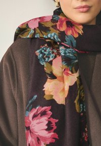 Blomstret tørklæde med en mørk baggrund og blomster i pink, orange og blå nuancer. Blødt stof falder elegant omkring skuldrene.