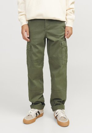 Enfant portant un pantalon cargo vert avec des poches latérales, des baskets blanches à semelles marron et un sweat-shirt couleur crème.