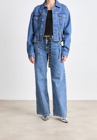 Ljusblå denimjacka med en croppad design, två bröstfickor och snörning vid fållen. Turad med högmidjade blå jeans.