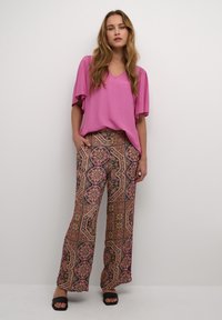 Top rosa de cuello en V con mangas cortas, combinado con pantalones anchos estampados que presentan intrincados diseños florales y geométricos en negro, rosa y dorado.