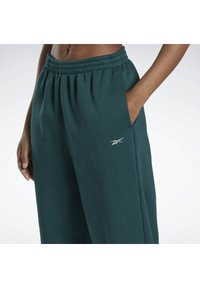 Turkosa, vida mjukisbyxor med elastisk midjeband, sidfickor och en liten vit logga på vänster lår. Mjuk tygstruktur.