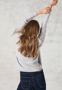 Jersey gris de punto con cuello redondo, combinado con jeans de denim azul oscuro que tienen bolsillos traseros y detalles de costura en contraste.